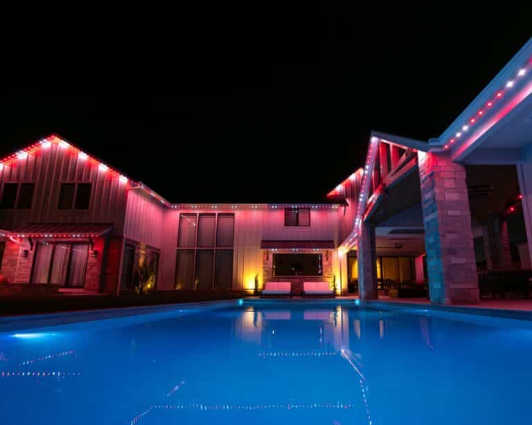 Red and white permanent lighting around a poolside residence